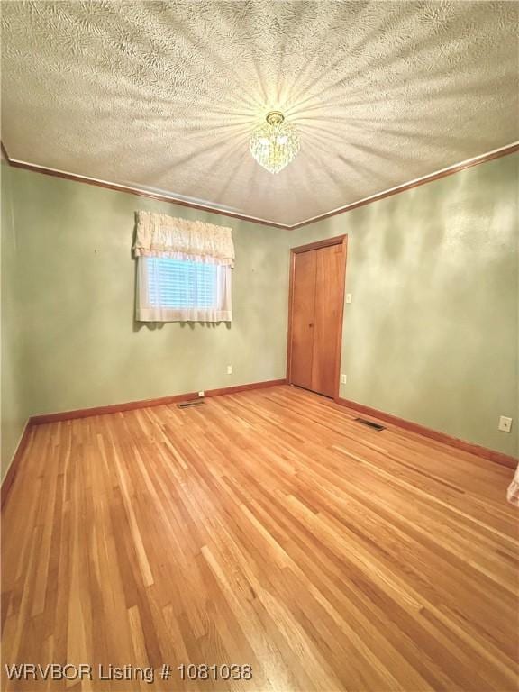 spare room featuring wood finished floors, ornamental molding, a chandelier, and a textured ceiling