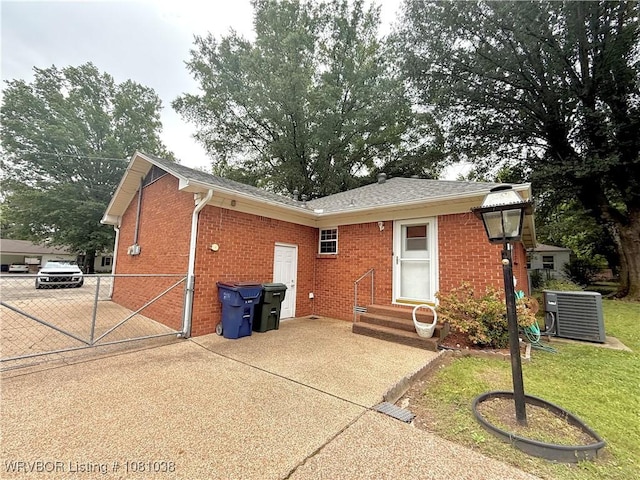 rear view of house featuring entry steps, brick siding, central air condition unit, and driveway