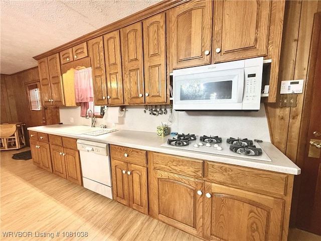 kitchen featuring white appliances, a sink, light wood finished floors, brown cabinets, and a textured ceiling