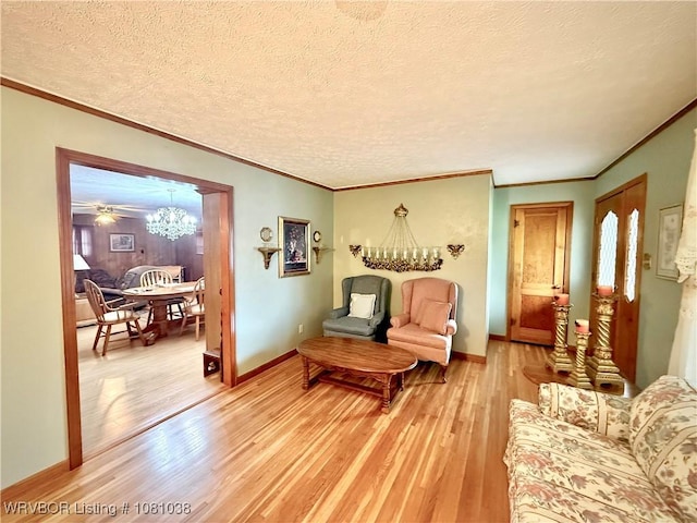 living room featuring light wood-style floors, a textured ceiling, a chandelier, baseboards, and crown molding