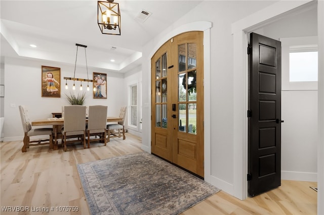 entrance foyer with a chandelier, light hardwood / wood-style floors, french doors, and a tray ceiling