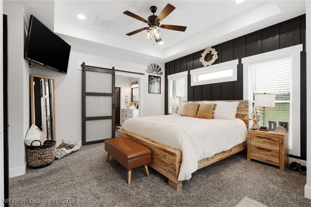 carpeted bedroom featuring a raised ceiling, a barn door, and ceiling fan