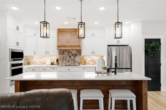 kitchen with hanging light fixtures, a center island with sink, white cabinets, and stainless steel appliances