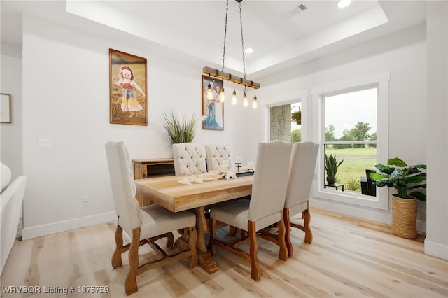 dining space with light wood-type flooring and a tray ceiling