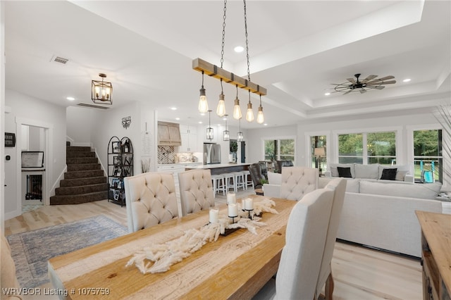 dining area with ceiling fan, light hardwood / wood-style floors, and a raised ceiling