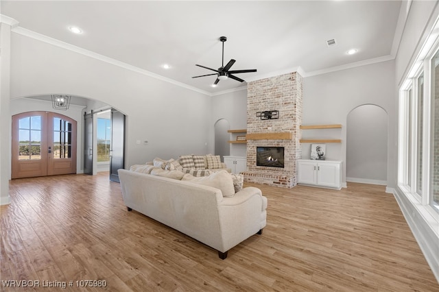 living room with ceiling fan, french doors, a brick fireplace, light hardwood / wood-style flooring, and ornamental molding