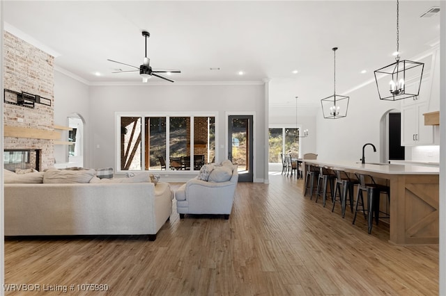 living room featuring ornamental molding, ceiling fan, sink, wood-type flooring, and a stone fireplace