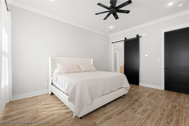 bedroom with a barn door, ceiling fan, light wood-type flooring, and ornamental molding