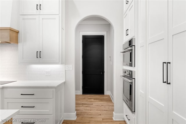 kitchen featuring white cabinets, light wood-type flooring, double oven, and tasteful backsplash