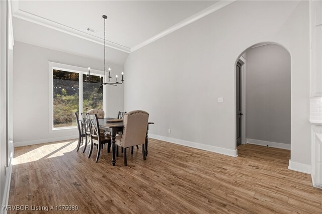 dining room with a chandelier, light hardwood / wood-style floors, vaulted ceiling, and ornamental molding