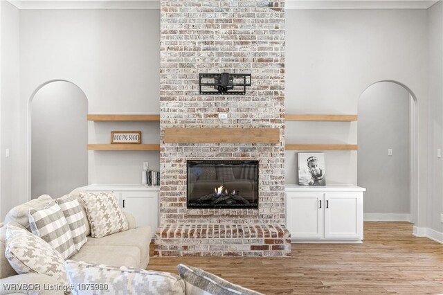 living room with a brick fireplace, light wood-type flooring, and built in features