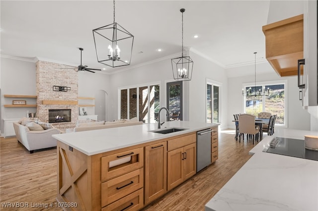 kitchen featuring a brick fireplace, stainless steel dishwasher, ceiling fan, pendant lighting, and an island with sink