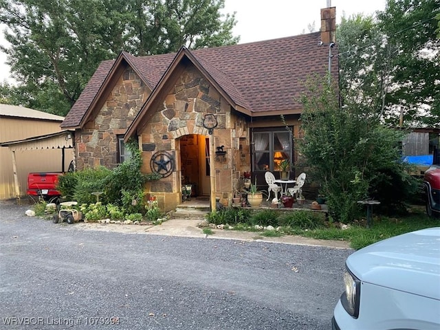 view of front facade with stone siding, a shingled roof, and a chimney