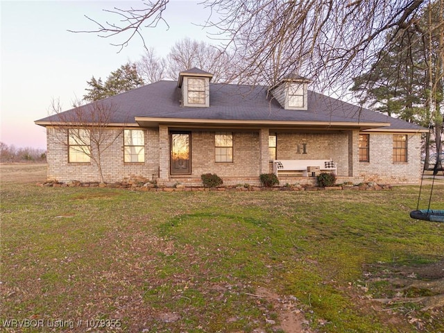 back of property at dusk with brick siding and a yard