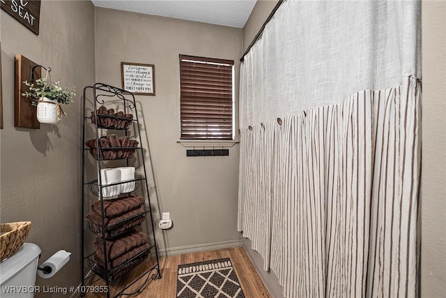 bathroom with toilet, a textured ceiling, baseboards, and wood finished floors