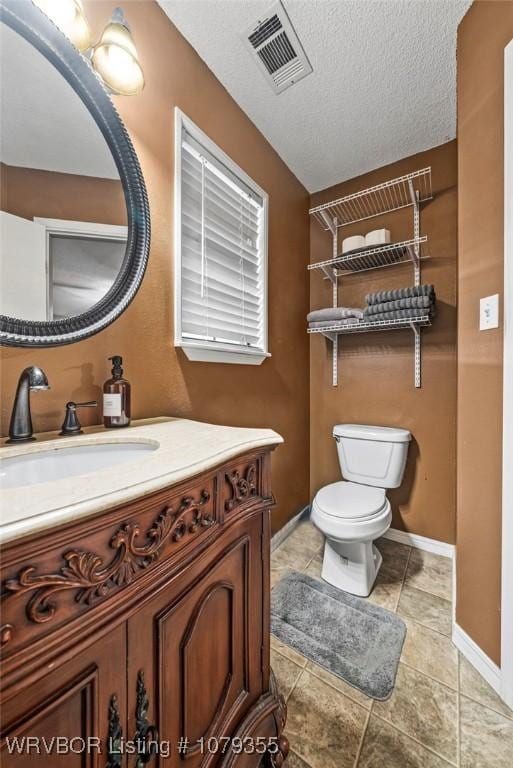 bathroom featuring a textured ceiling, toilet, vanity, visible vents, and baseboards