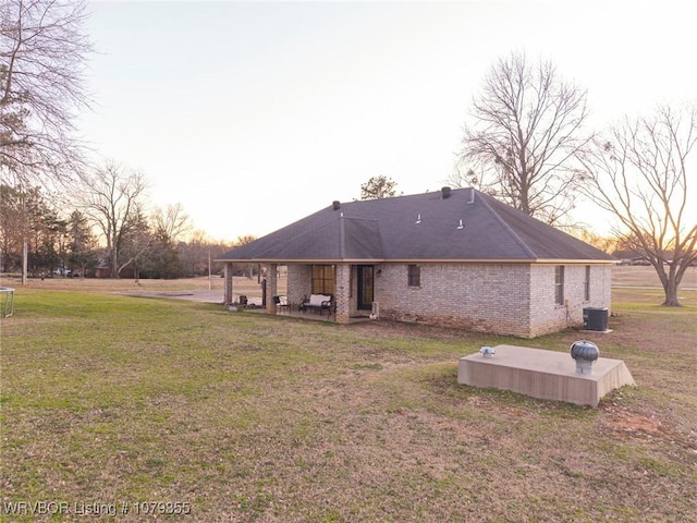 back of property featuring a trampoline, brick siding, a yard, central AC unit, and a patio area