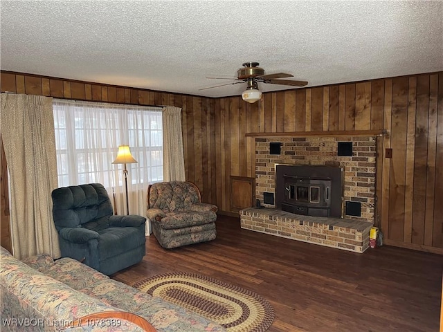 living room featuring ceiling fan, dark hardwood / wood-style flooring, wooden walls, a wood stove, and a textured ceiling