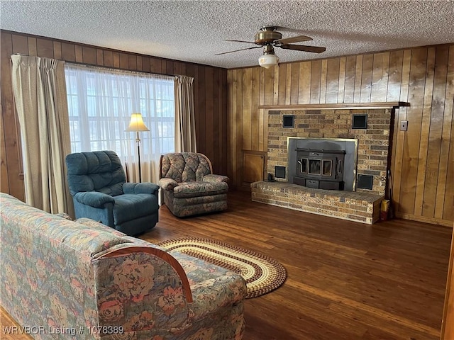 living room featuring wood walls, ceiling fan, a wood stove, and hardwood / wood-style floors