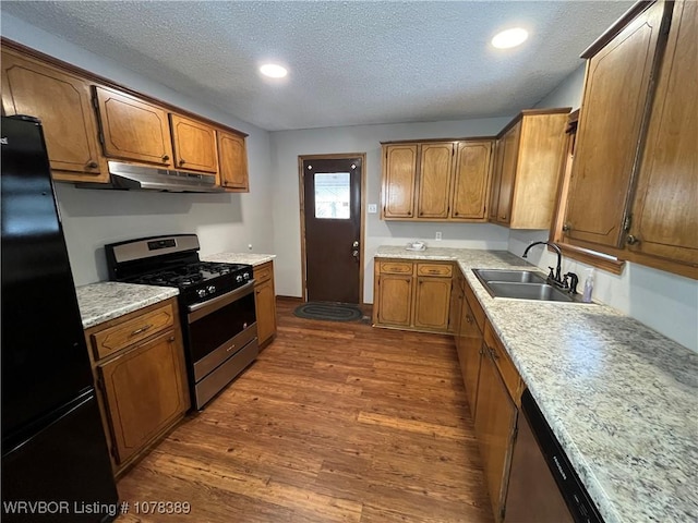 kitchen with a textured ceiling, black refrigerator, stainless steel gas stove, dark hardwood / wood-style flooring, and sink