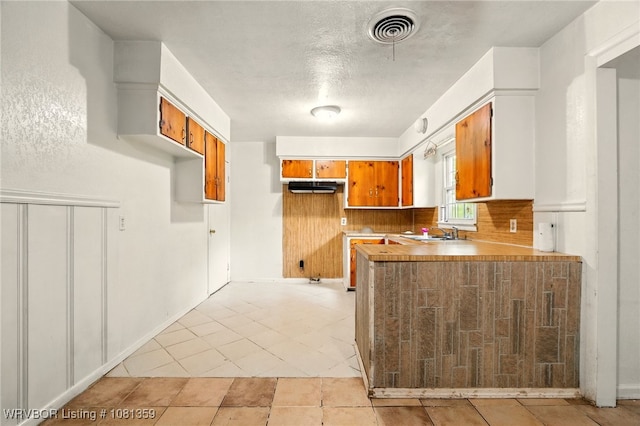 4002 57th St, Fort Smith, AR 72904 - kitchen with brown cabinetry, extractor fan, a peninsula, light countertops, and light tile patterned floors
