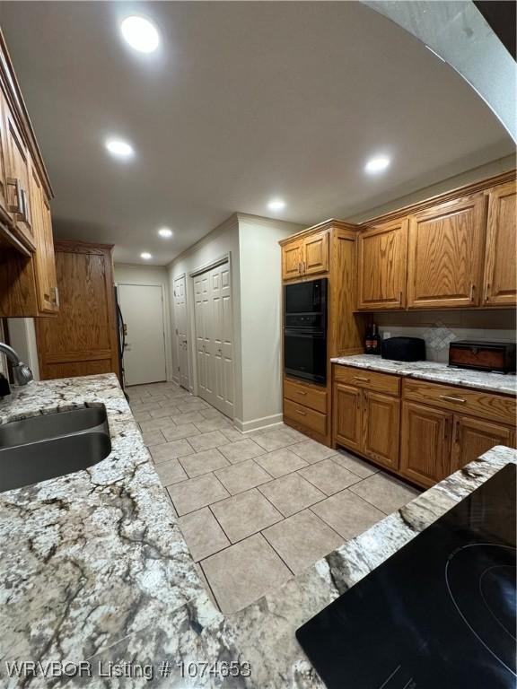 kitchen with light stone countertops, sink, light tile patterned floors, and black appliances