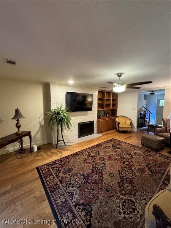 living room with ceiling fan, a large fireplace, hardwood / wood-style floors, and a textured ceiling