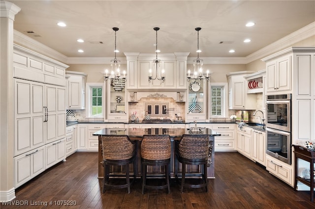 kitchen with backsplash, pendant lighting, a center island with sink, white cabinetry, and a breakfast bar area