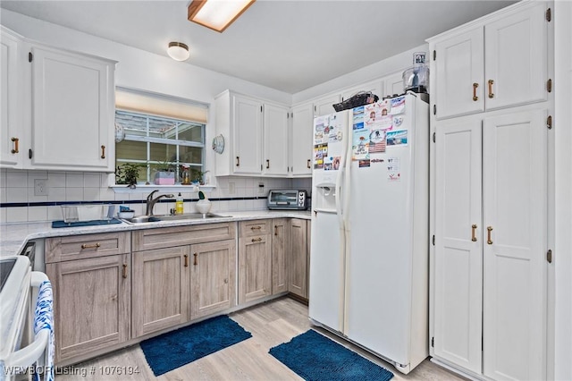 kitchen featuring sink, tasteful backsplash, white refrigerator with ice dispenser, white cabinets, and range