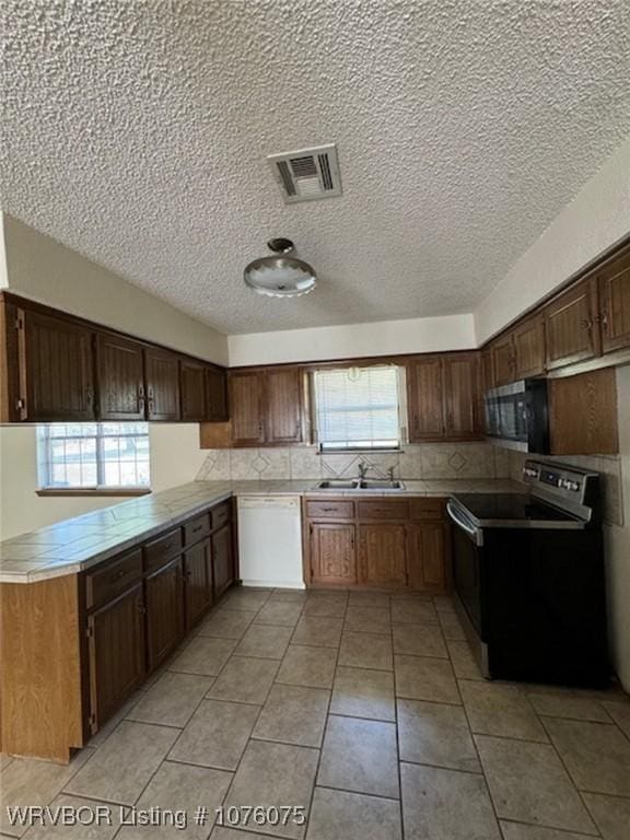 kitchen with kitchen peninsula, white dishwasher, sink, light tile patterned floors, and black range with electric stovetop