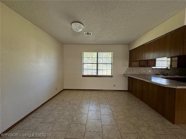 kitchen with decorative backsplash, light tile patterned floors, a textured ceiling, and kitchen peninsula