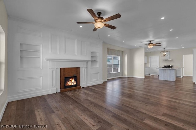 unfurnished living room featuring baseboards, built in shelves, a lit fireplace, and dark wood-style flooring