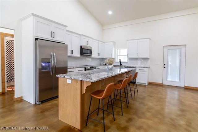 kitchen featuring white cabinets, a kitchen island, a kitchen bar, stainless steel appliances, and high vaulted ceiling