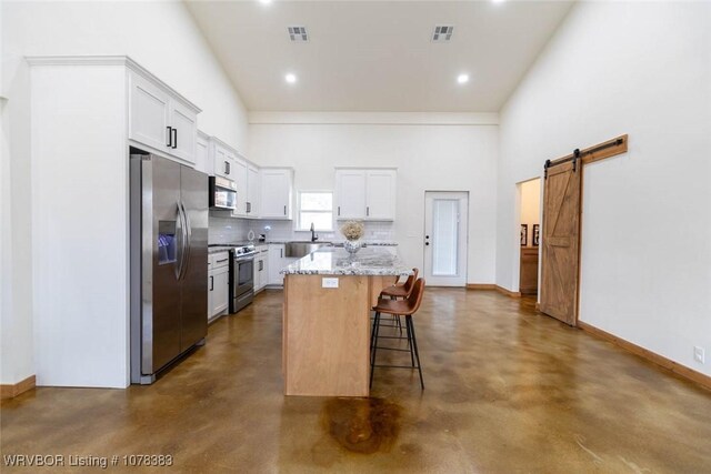 kitchen with a center island, stainless steel appliances, a kitchen breakfast bar, high vaulted ceiling, and a barn door