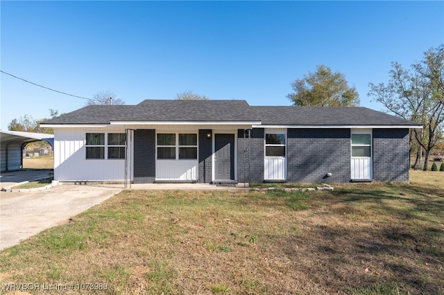 ranch-style home with a shingled roof, concrete driveway, a detached carport, a front yard, and brick siding