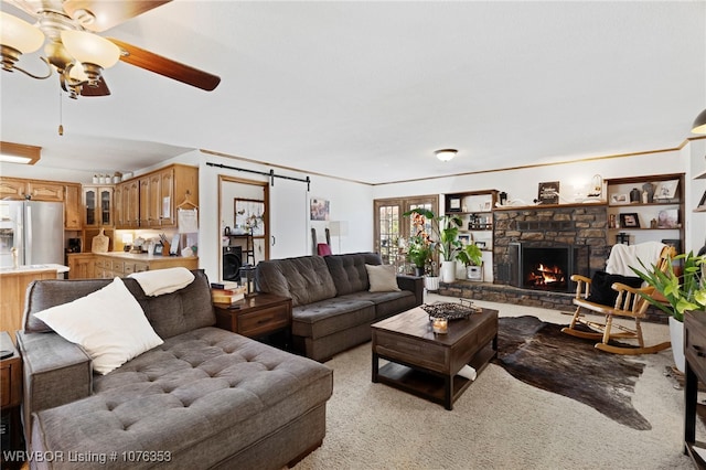 carpeted living room with a fireplace, a barn door, and ceiling fan