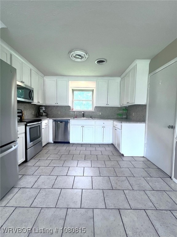 kitchen with a sink, stainless steel appliances, decorative backsplash, and white cabinets
