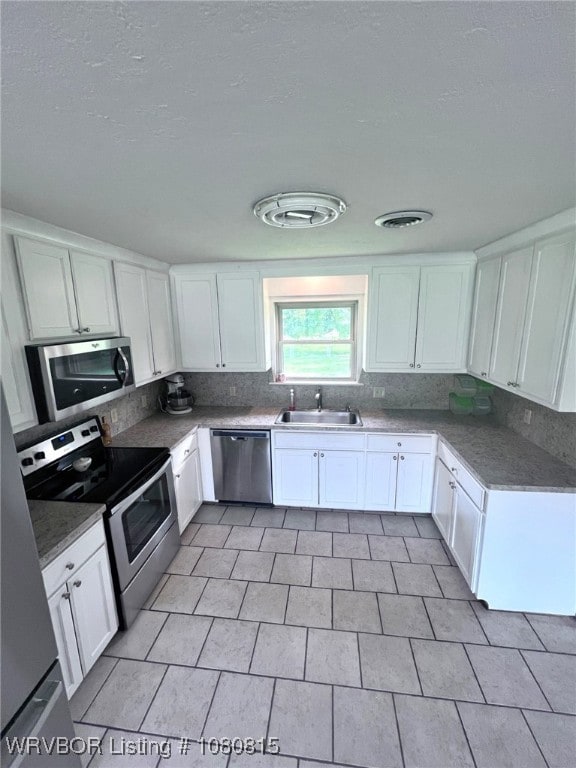 kitchen featuring a sink, a textured ceiling, white cabinetry, backsplash, and appliances with stainless steel finishes