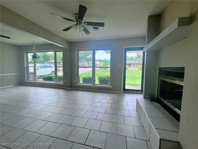 unfurnished living room with visible vents, tile patterned floors, a ceiling fan, baseboards, and a glass covered fireplace