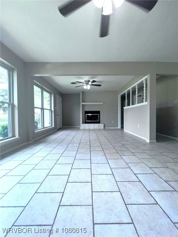 unfurnished living room featuring light tile patterned flooring, baseboards, a ceiling fan, and a fireplace