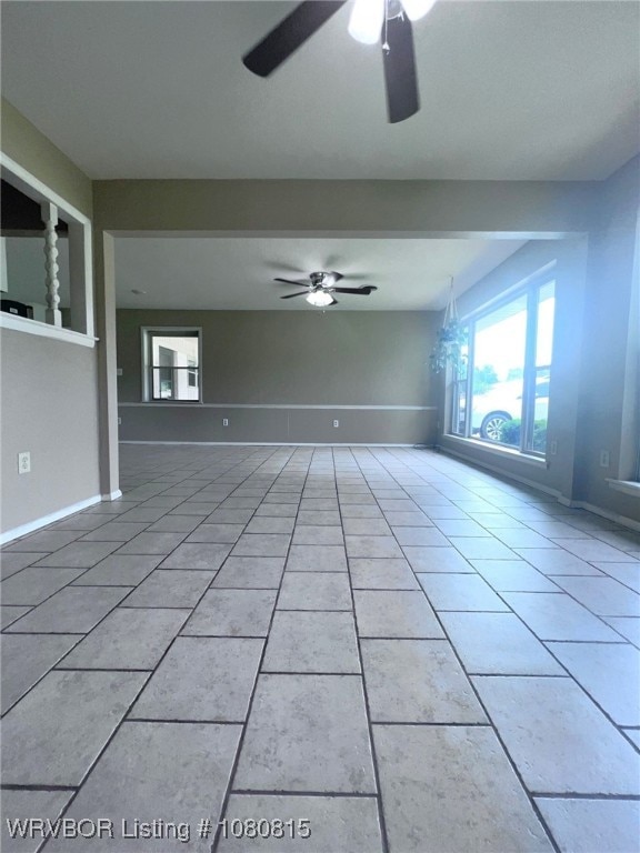 tiled empty room featuring baseboards and ceiling fan