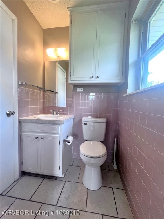 half bathroom with tile walls, toilet, vanity, a textured ceiling, and tile patterned flooring