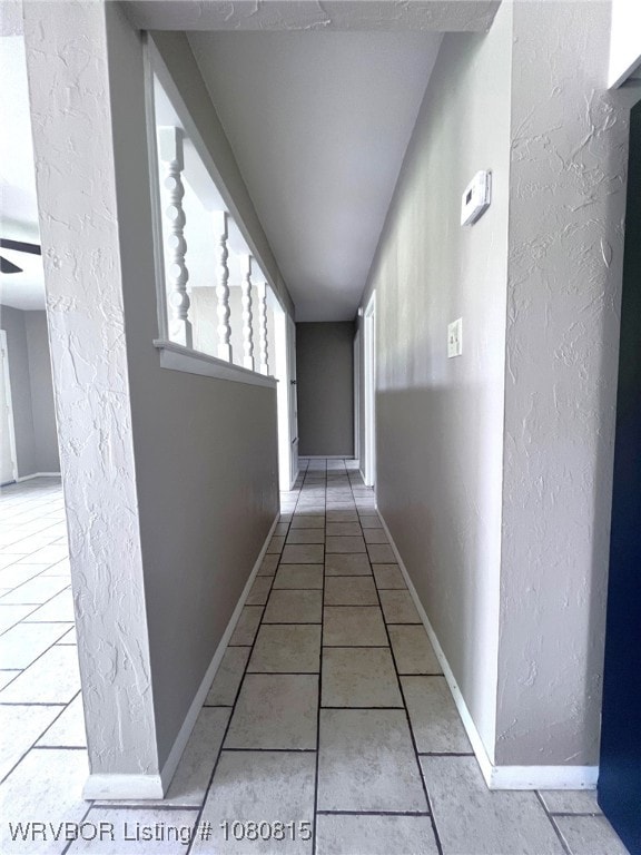 hallway featuring baseboards, tile patterned floors, and a textured wall