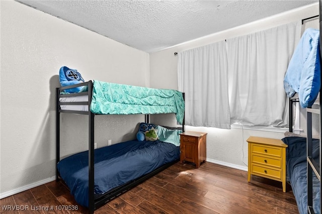 bedroom with a textured wall, a textured ceiling, baseboards, and wood finished floors