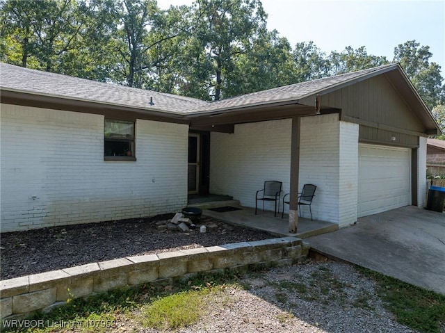 doorway to property with brick siding, an attached garage, concrete driveway, and roof with shingles