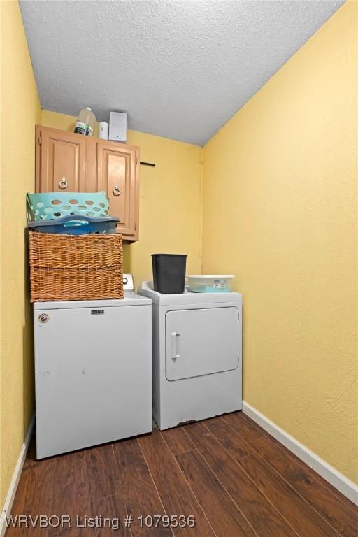 clothes washing area with dark wood-type flooring, a textured ceiling, cabinet space, baseboards, and washing machine and clothes dryer