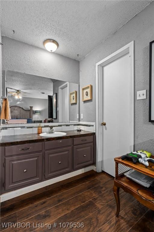 bathroom featuring vanity, wood finished floors, a textured wall, and a textured ceiling