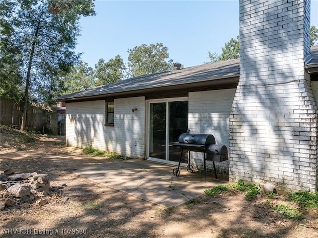 rear view of property featuring brick siding, a patio area, a shingled roof, and fence