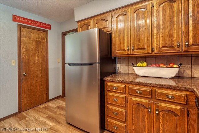 3001 Coral Cir, Alma, AR 72921 - kitchen with freestanding refrigerator, light wood-type flooring, decorative backsplash, brown cabinets, and a textured ceiling