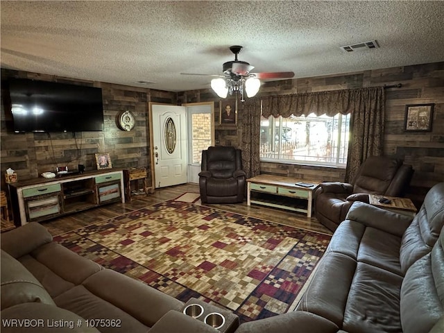 living room with wooden walls, ceiling fan, and a textured ceiling